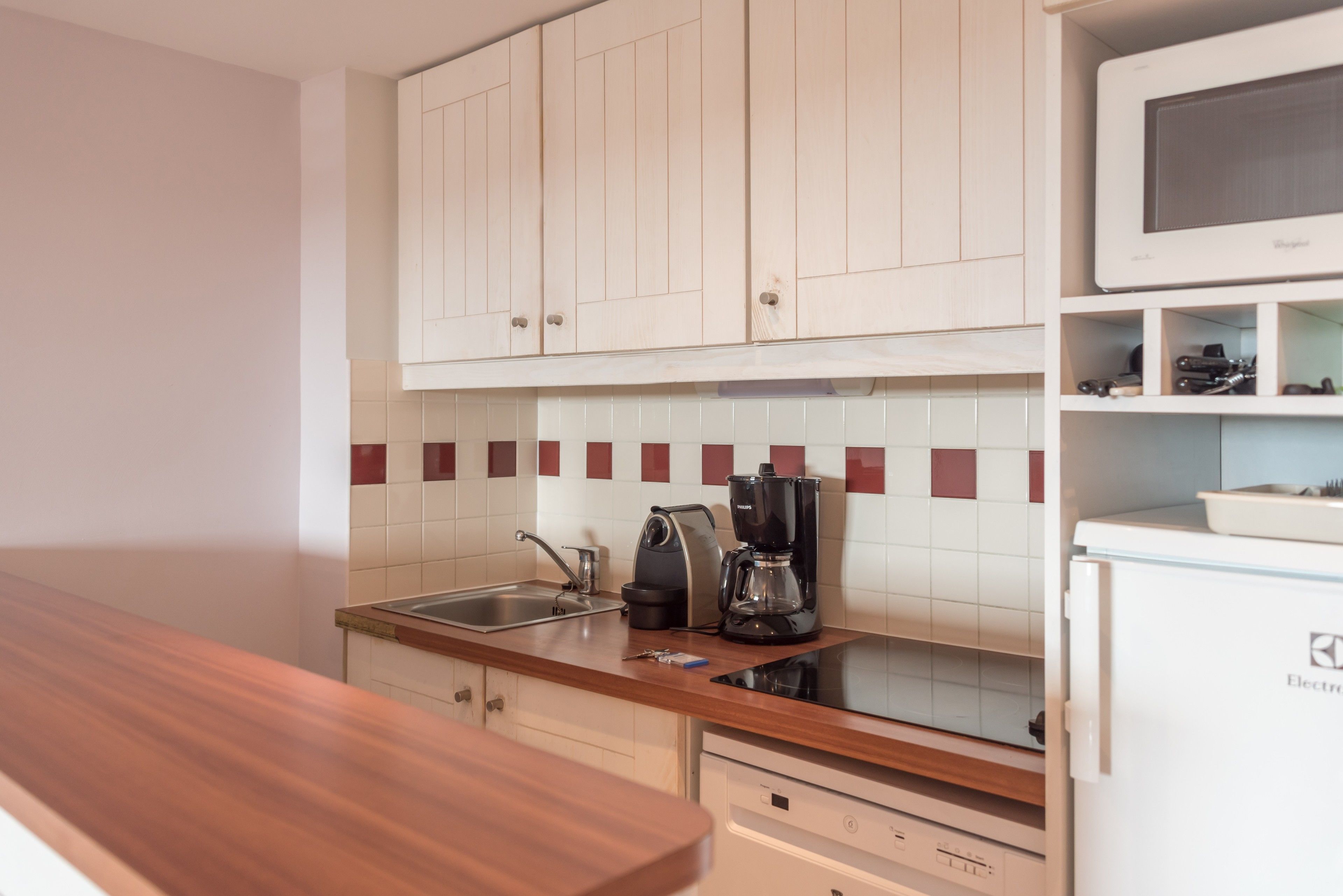 Una cocina con armarios de madera, microondas, cafetera y refrigerador.