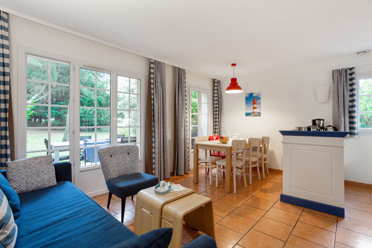 Una sala de estar moderna con un sofá, sillas, una mesa de comedor y una zona de cocina con mostrador.