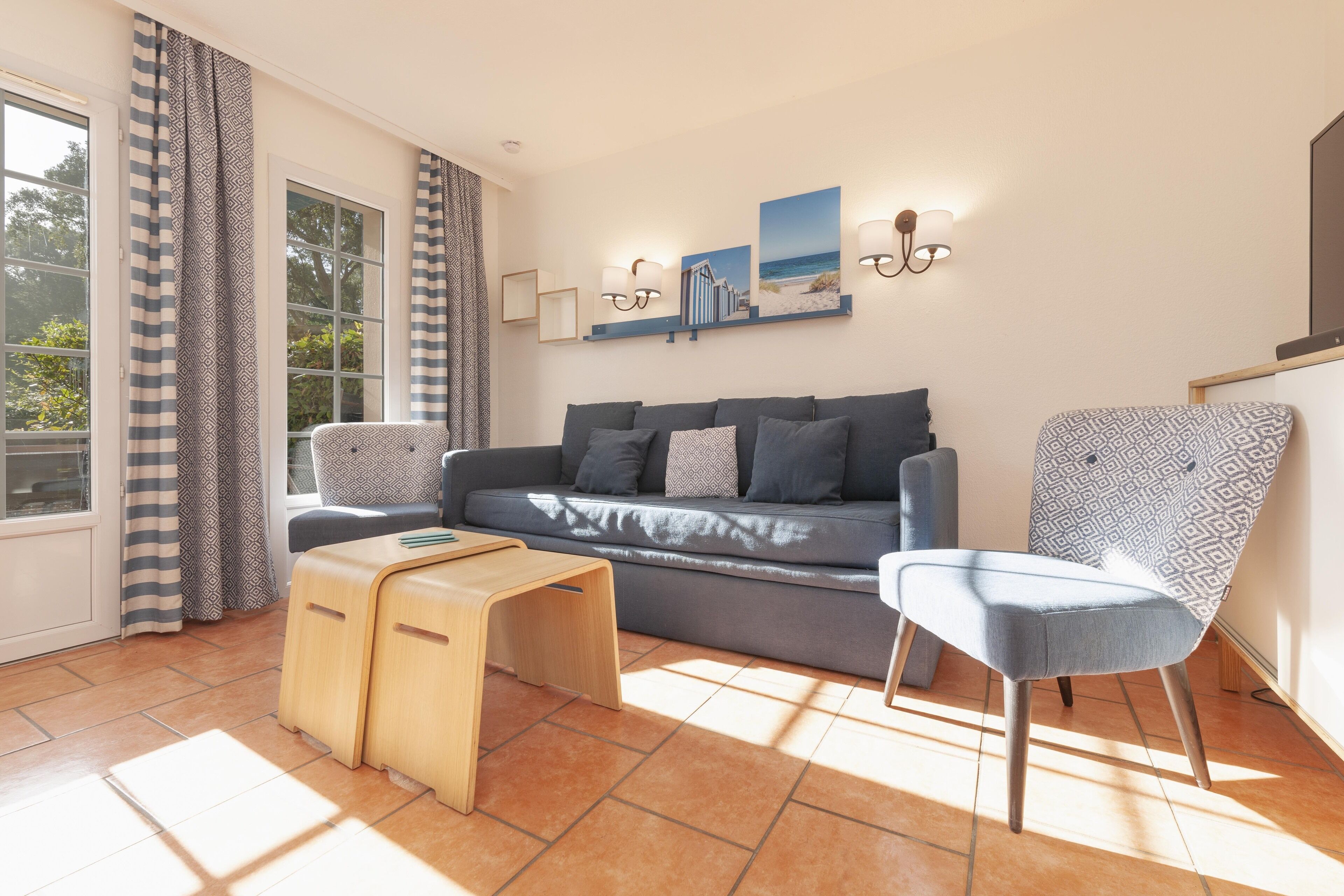 Un salon moderne avec un canapé gris, des coussins à motifs, une table d’appoint en bois et un fauteuil à motifs.