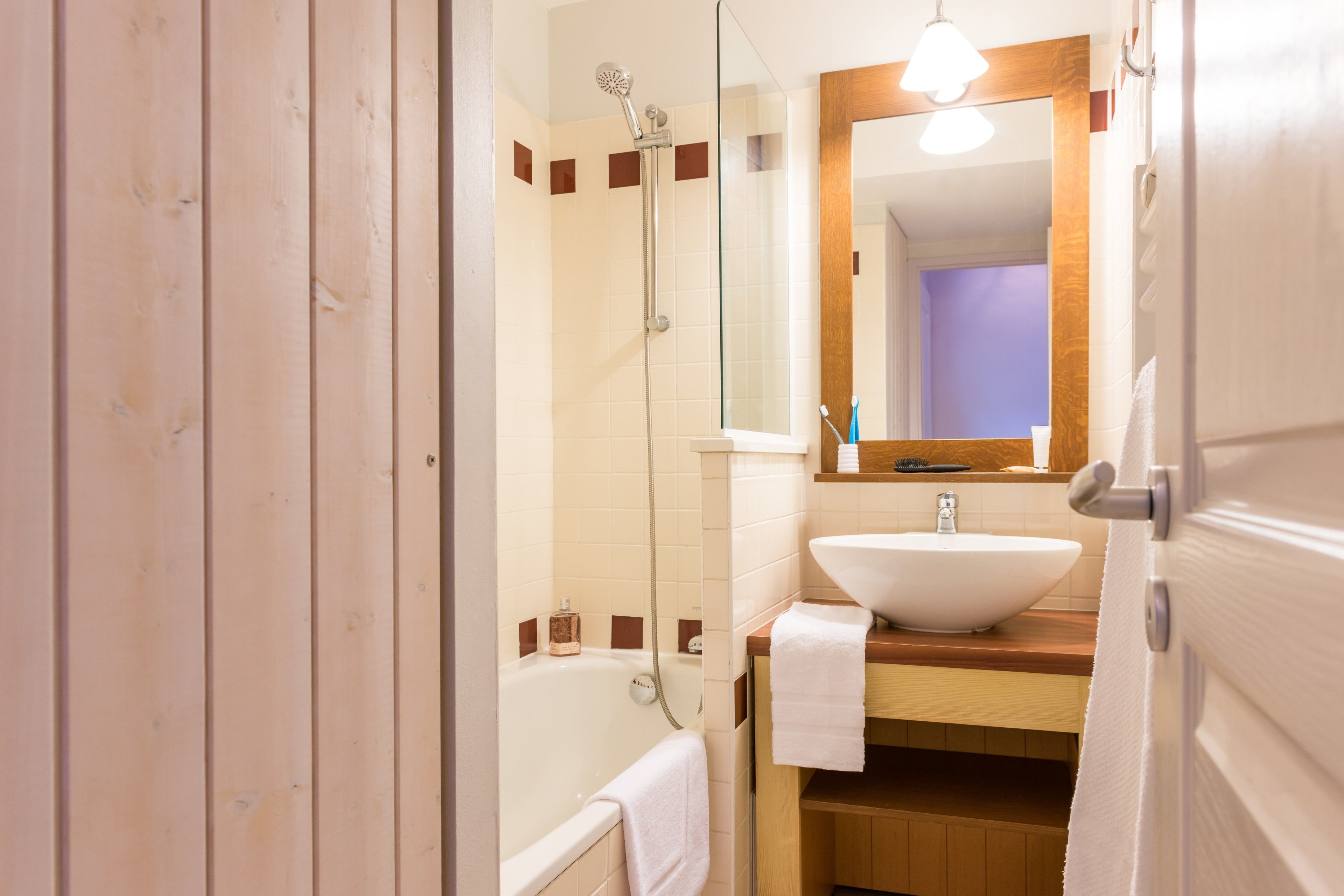 A bathroom with a wooden door, a white bathtub, a sink with a mirror above it, and a shower area.