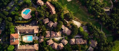 Vista aérea de un complejo turístico con varias cabañas, una piscina y abundante vegetación.
