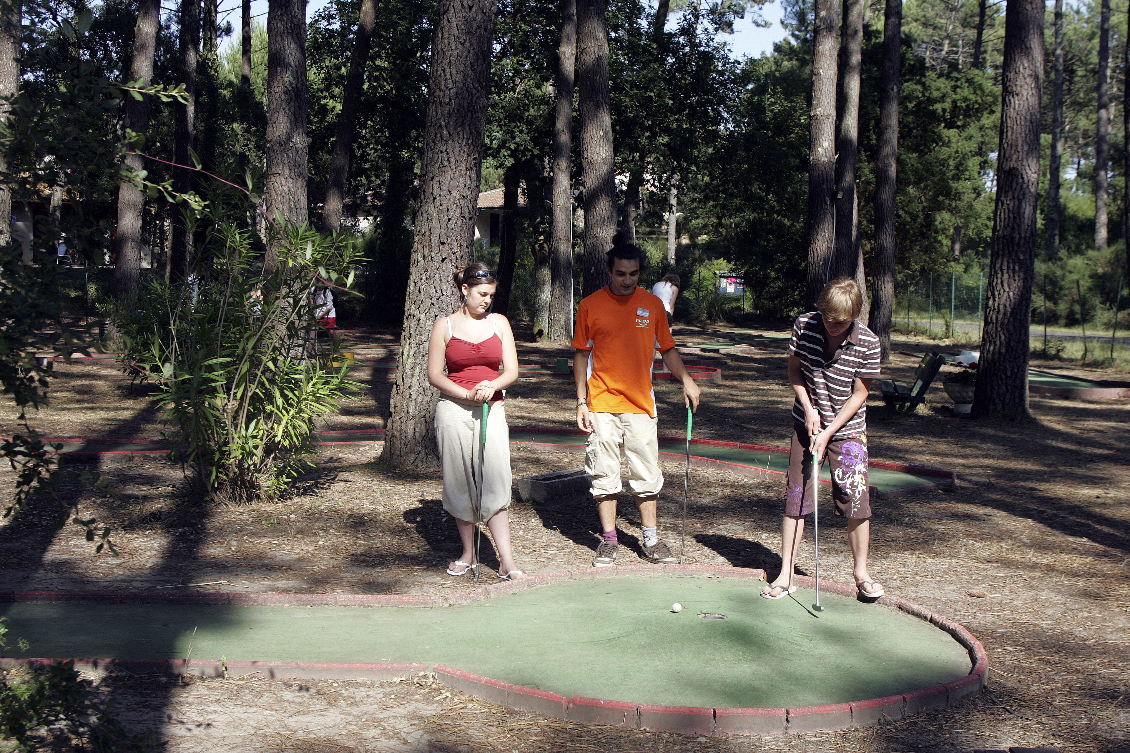 Três pessoas jogando golfe em um campo cercado por árvores.