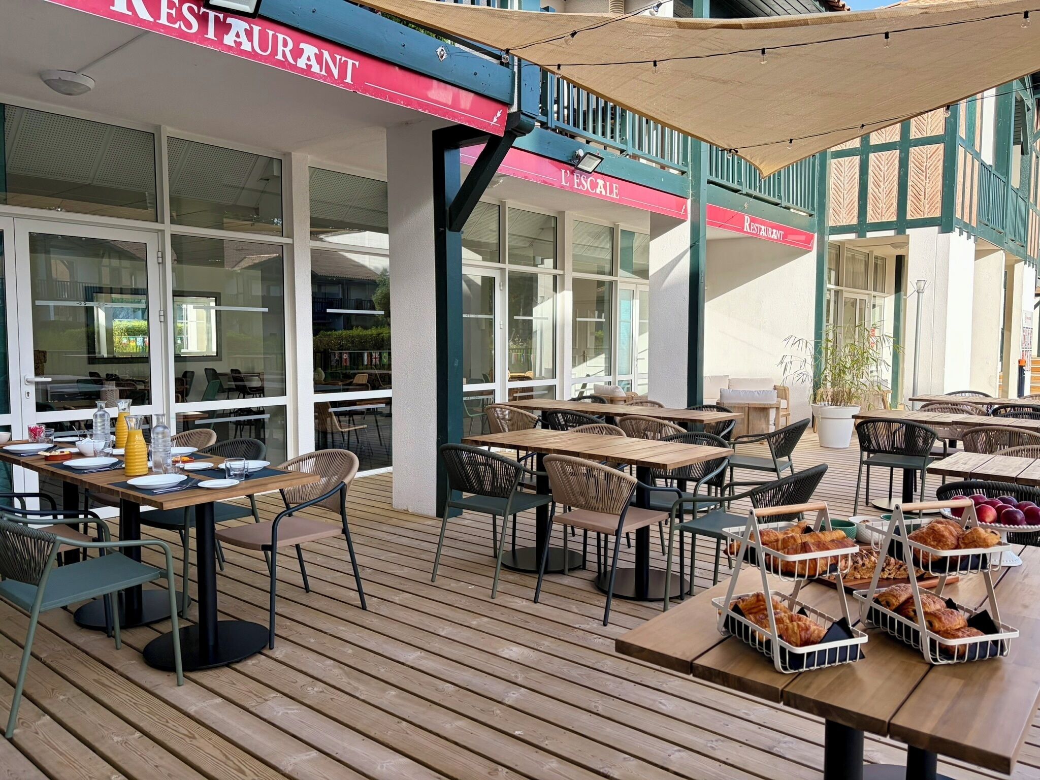 An outdoor dining area with tables and chairs, a sign for a restaurant, and a view of the building's interior.