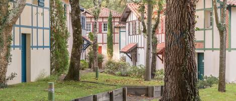 Un patio con edificios de estilo europeo tradicional, un sendero central y abundante vegetación.