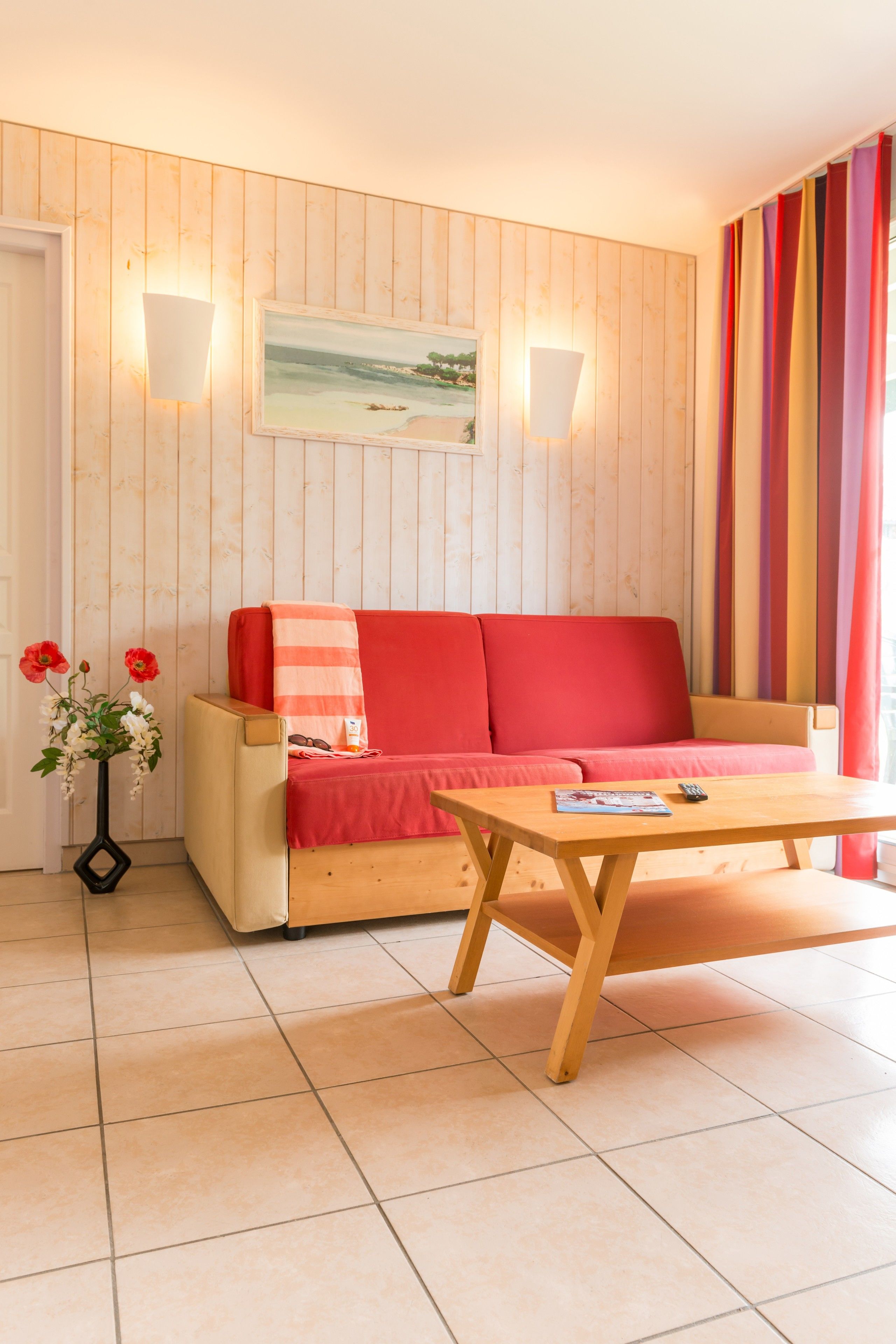 Une pièce chaleureuse avec un mur lambrissé en bois, un canapé rouge, une table basse en bois et un tableau représentant une scène de plage.