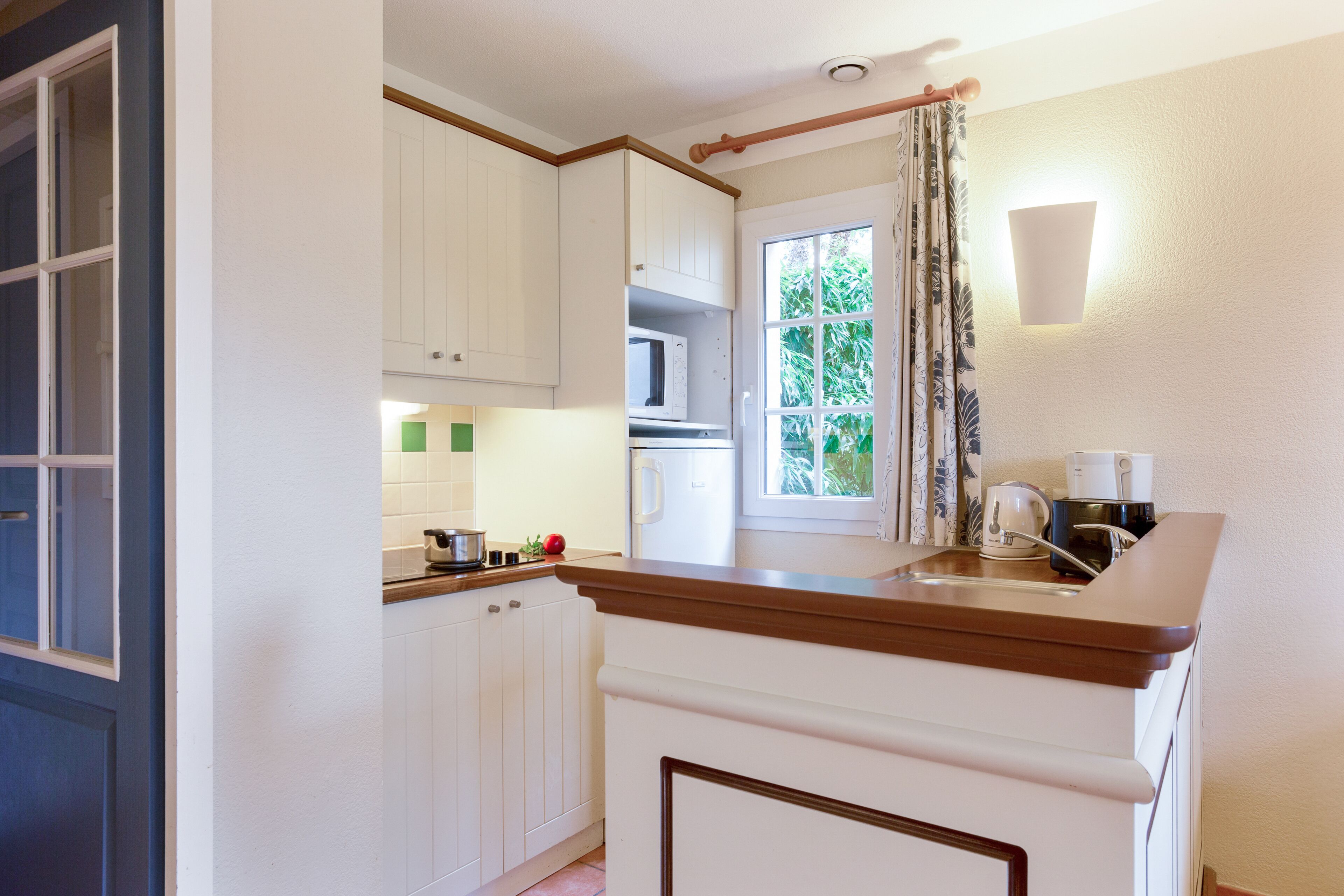 A kitchen with white cabinets, a microwave, a refrigerator, and a window with curtains.
