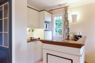 A kitchen with white cabinets, a microwave, a refrigerator, and a window with curtains.