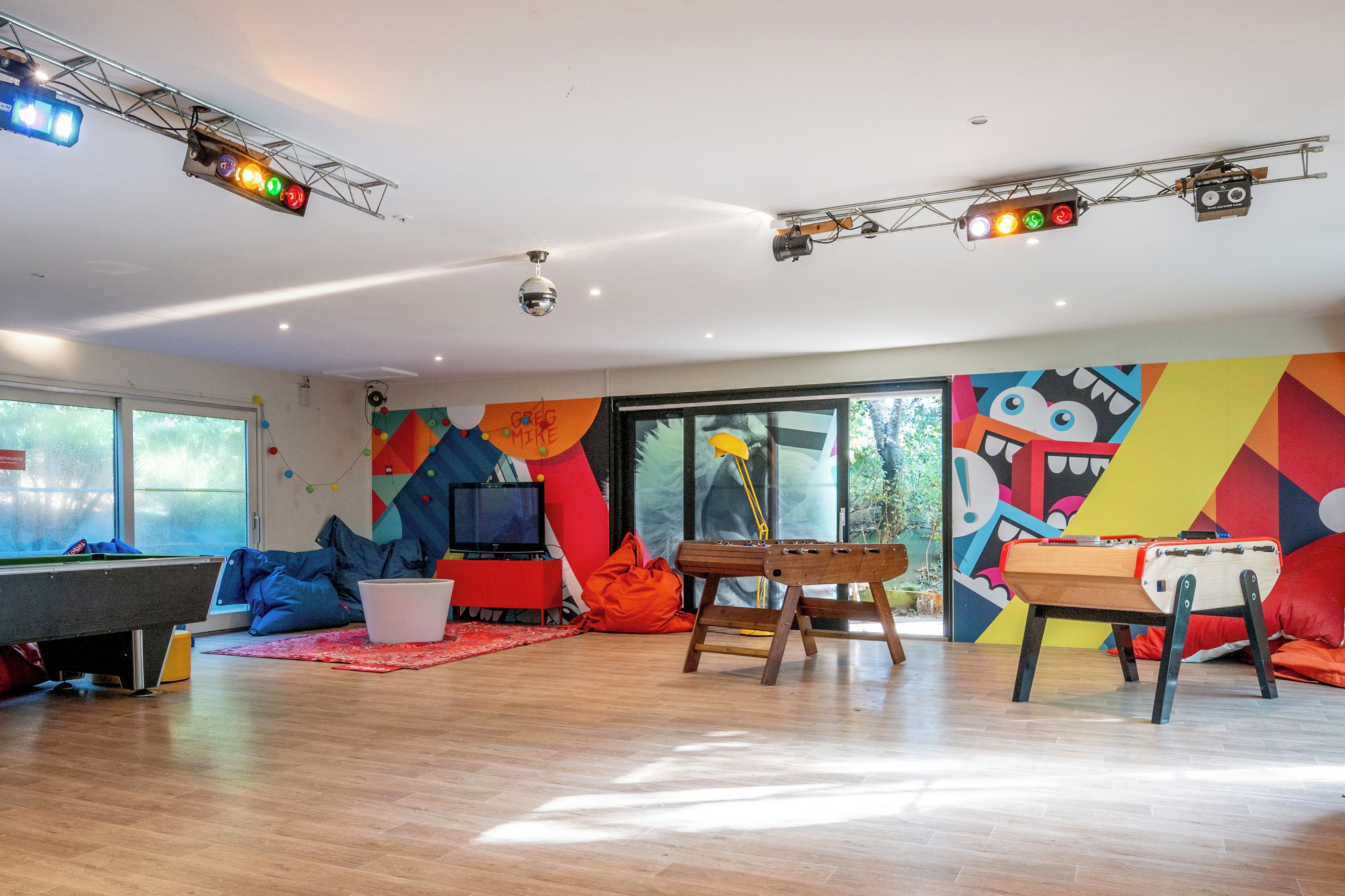 A spacious room with a pool table, a television, and a colorful mural on the wall.