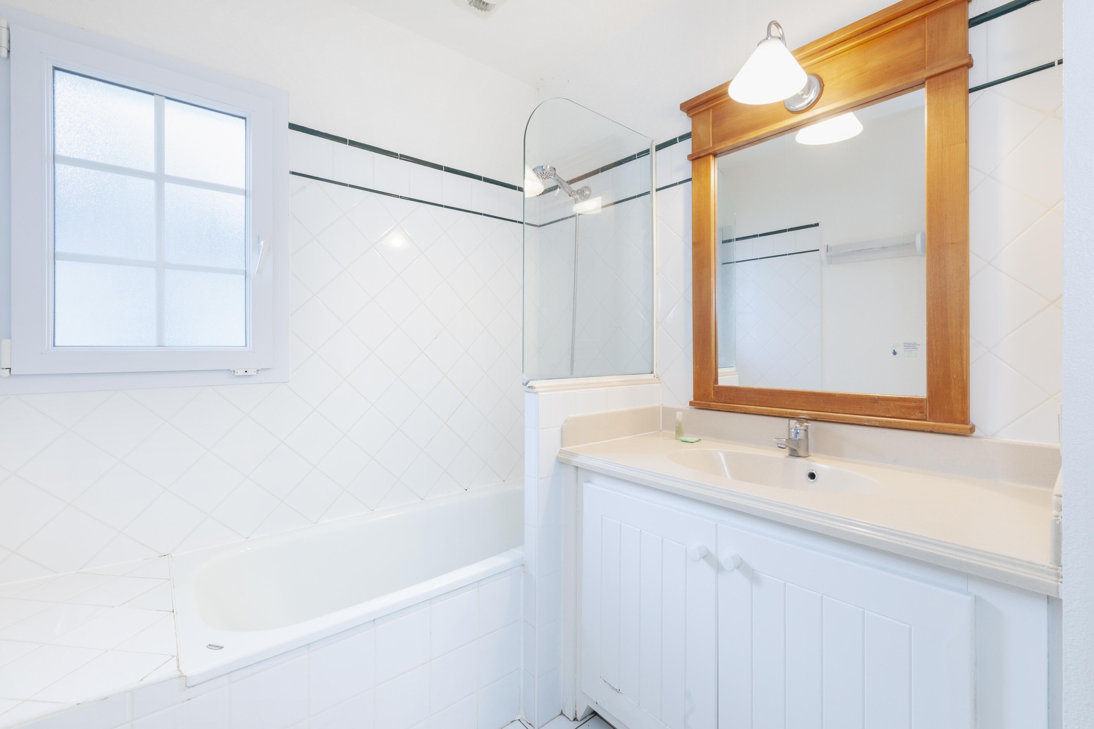 A bathroom with a bathtub, a sink, a mirror, and a window.