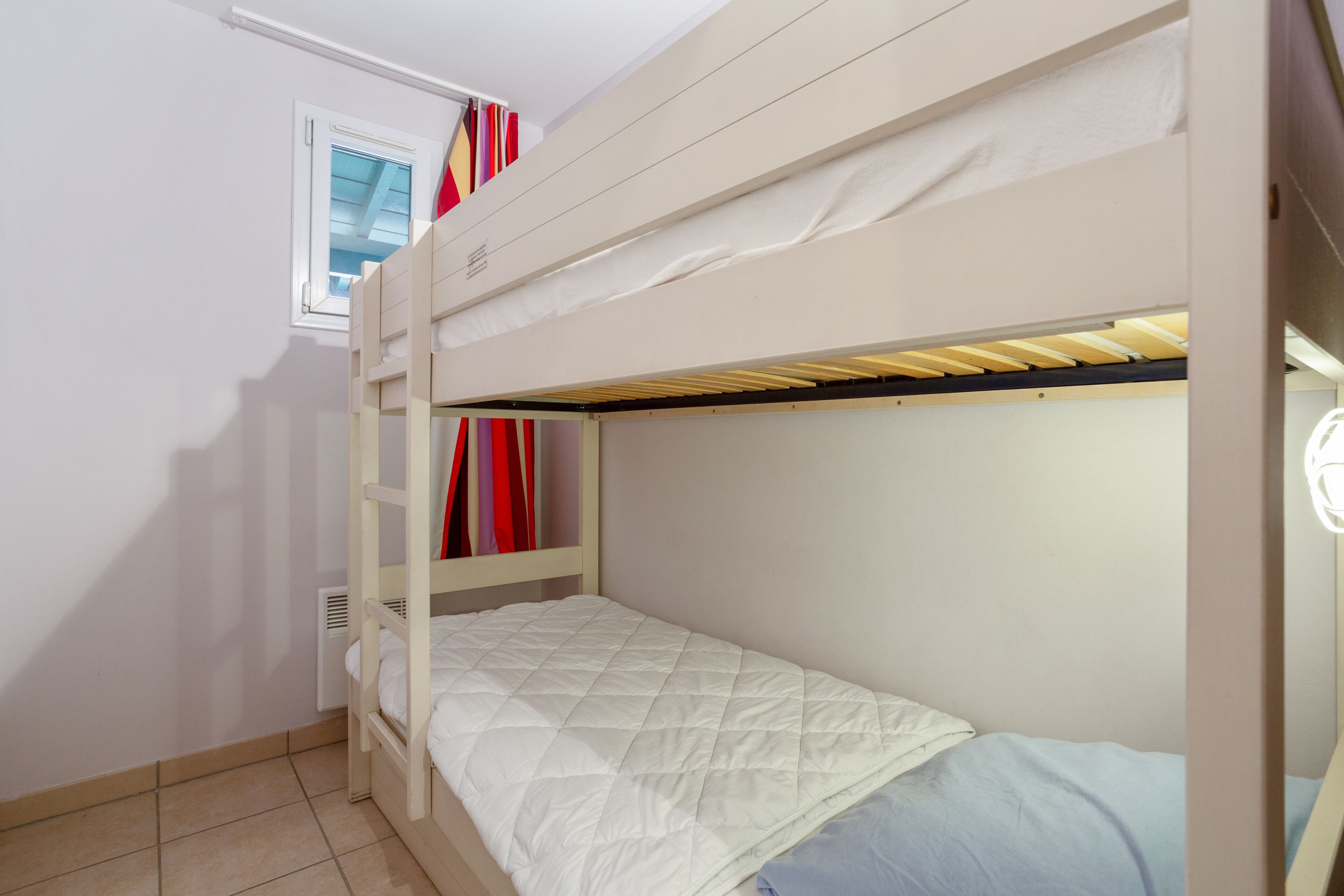 Une chambre avec un lit superposé, une fenêtre, un radiateur et une porte.