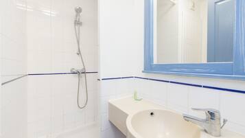 Un baño con paredes de azulejos blancos, un lavamanos color beige, un espejo con marco azul y una ducha con cabezal de ducha de mano.