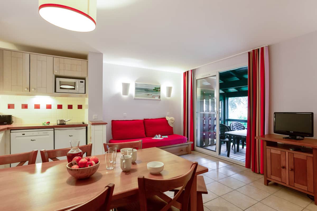 Una cocina moderna con comedor, un sofá rojo y un televisor sobre un mueble de madera.