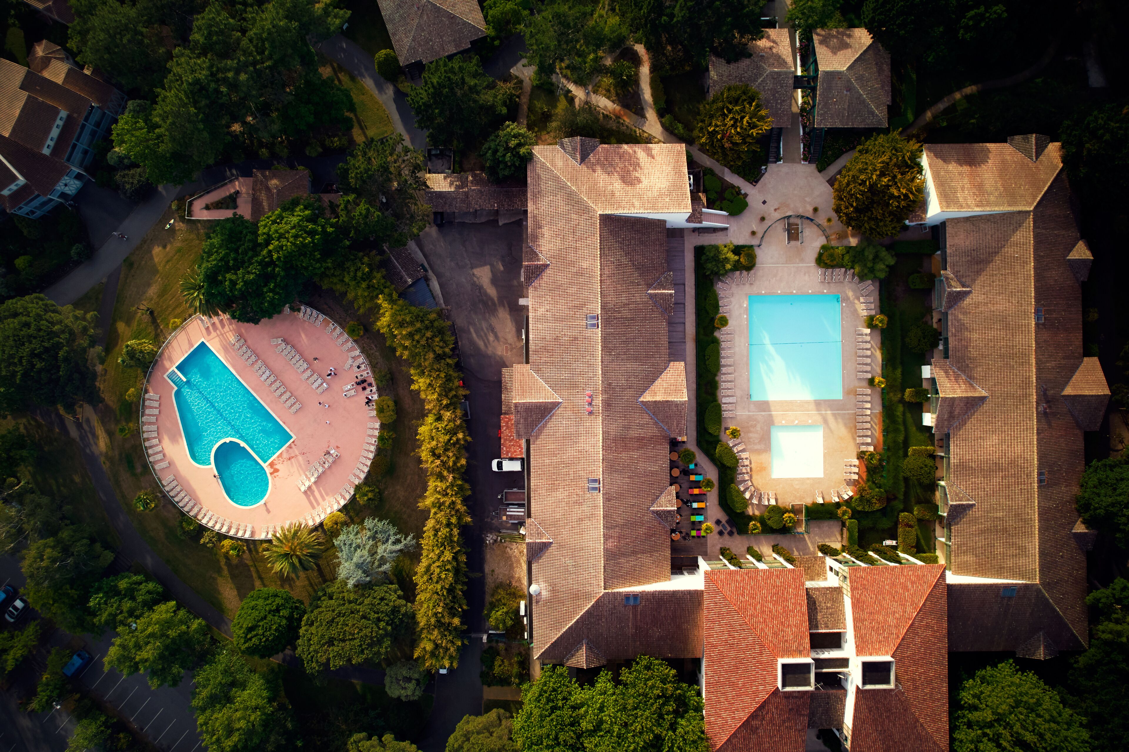 Vue aérienne d’un quartier résidentiel avec une piscine, un court de tennis et un jardin bien entretenu.