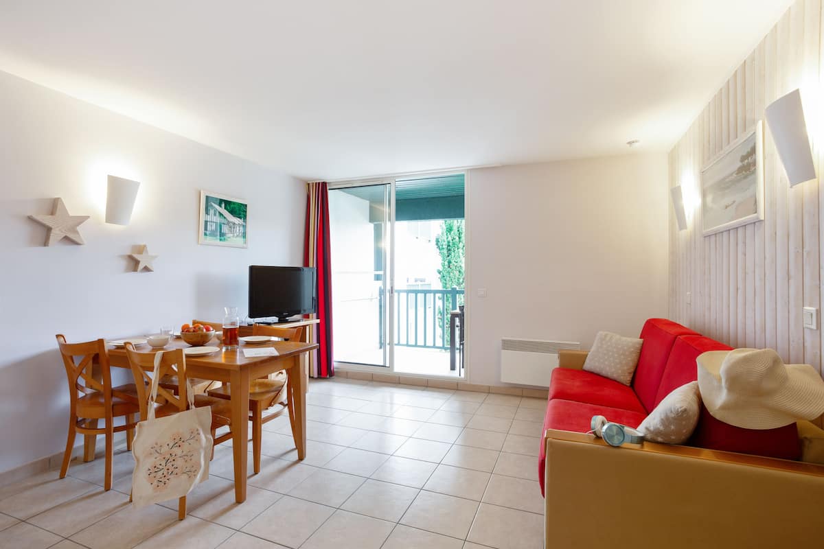 Una habitación con una mesa de comedor, sillas, un televisor, un sofá rojo y un balcón con una cortina roja.