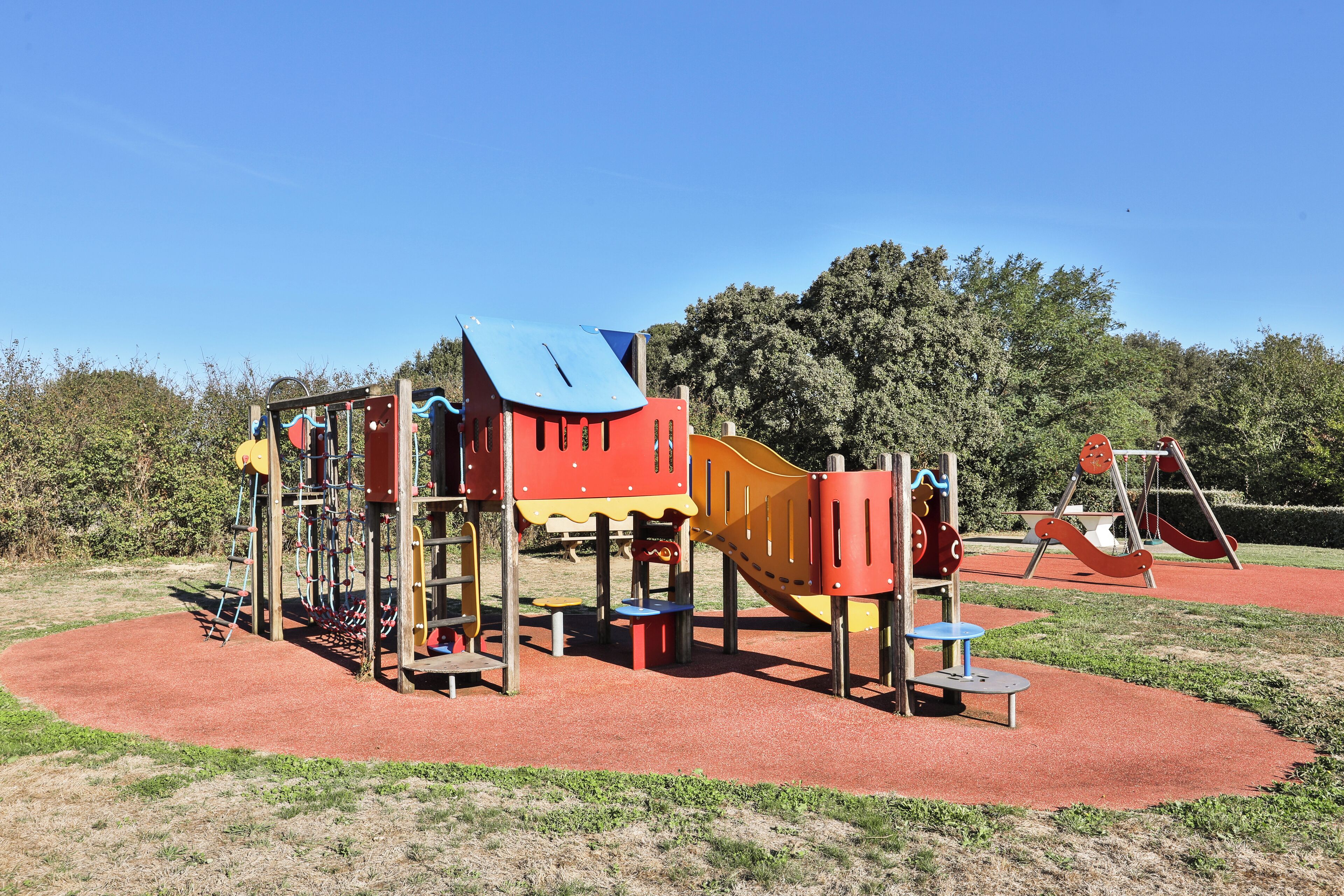 A playground with a slide, climbing structures, and a red rubberized surface.