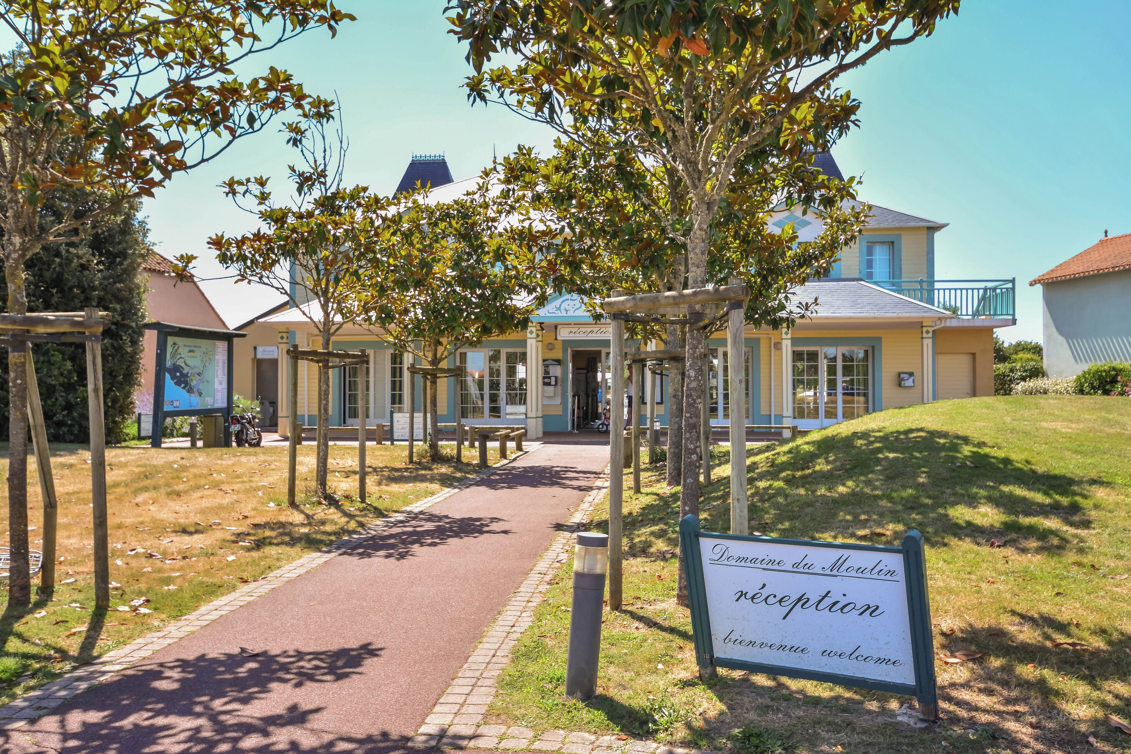 A reception area with a pathway leading to a building, surrounded by trees and a grassy area.