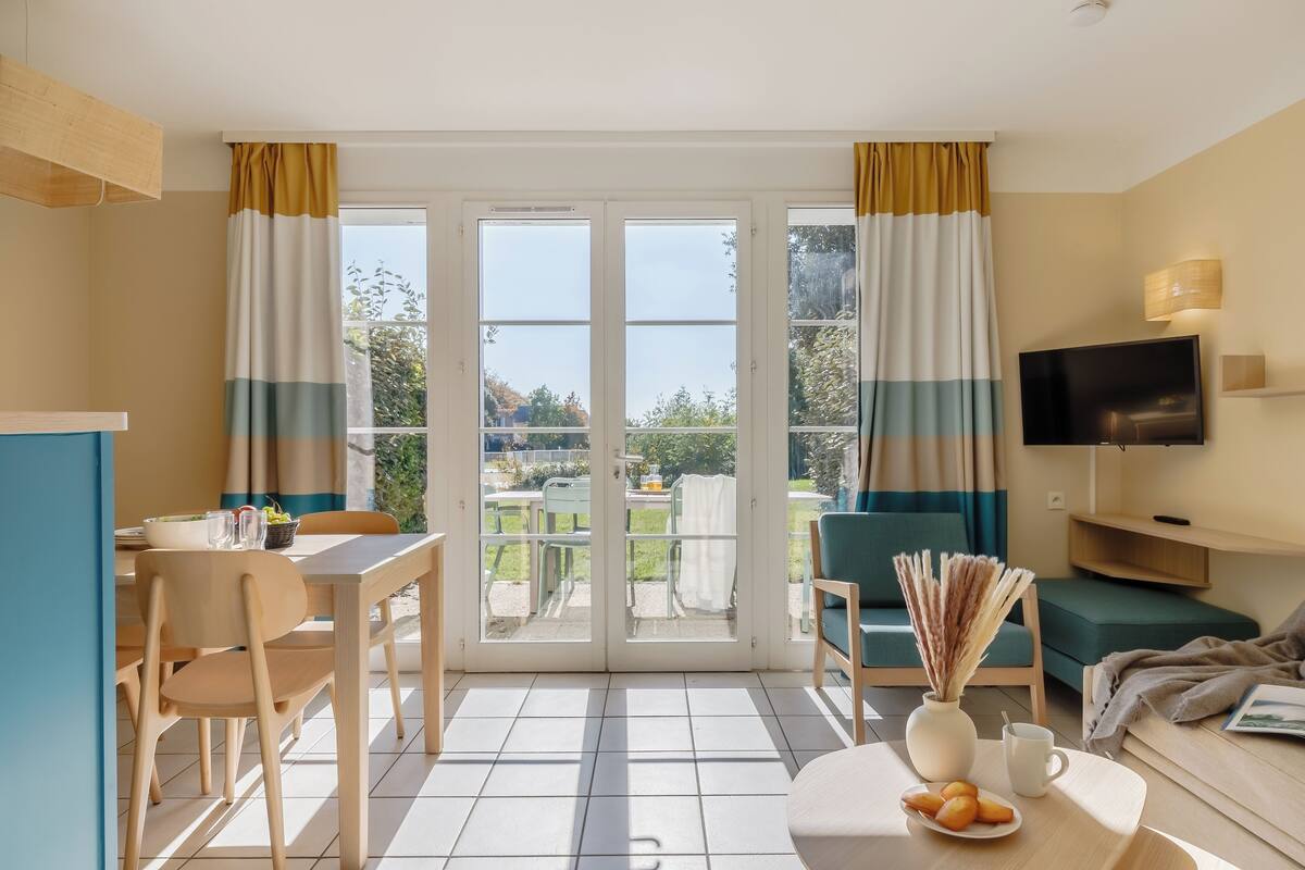 Een moderne woonkamer met een televisie, zithoek en een eettafel.