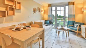 A modern living room with a wooden dining table, a sofa, and a TV cabinet. - Résidence Pierre & Vacances Le Domaine de Bourgenay (Talmont-Saint-Hilaire)