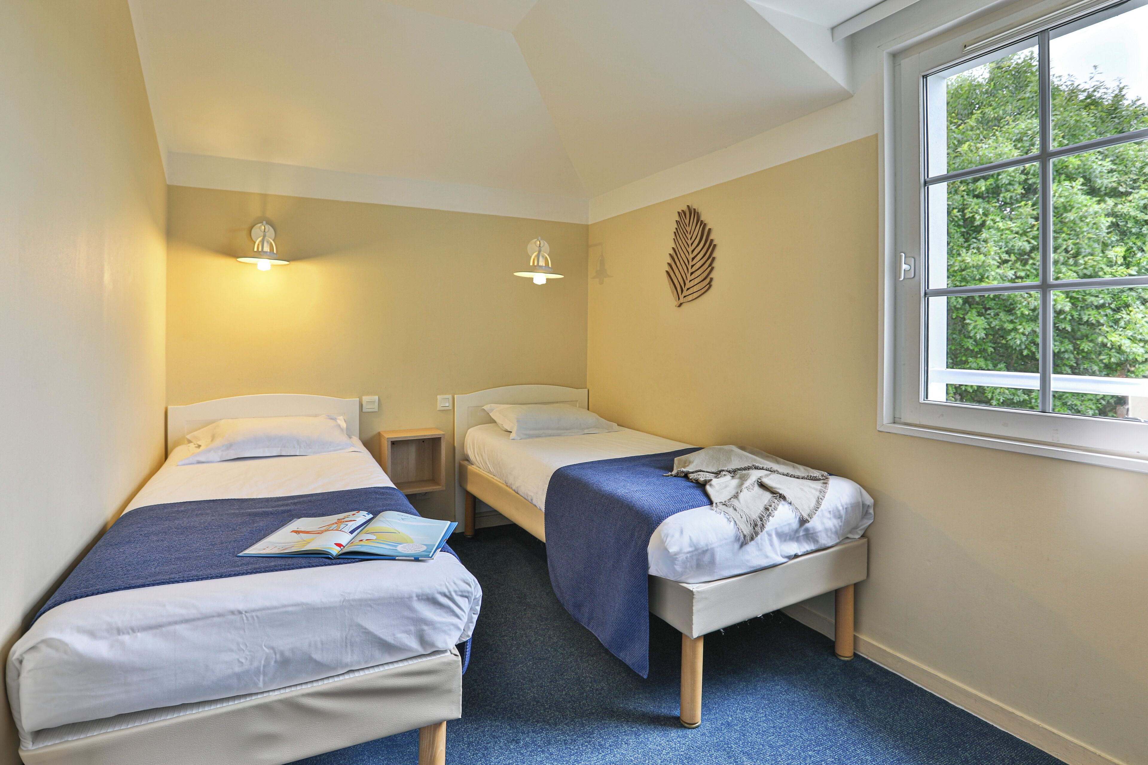 A room with two single beds, a window, and a wall-mounted light fixture.