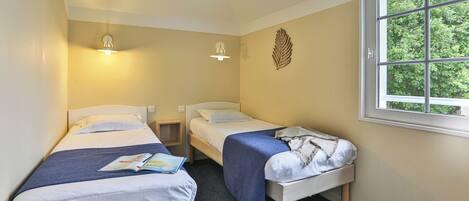 A room with two single beds, a window, and a wall-mounted light fixture.