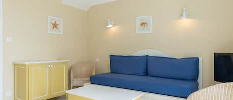 A room with a blue sofa, a yellow cabinet, a wicker chair, and a white table.