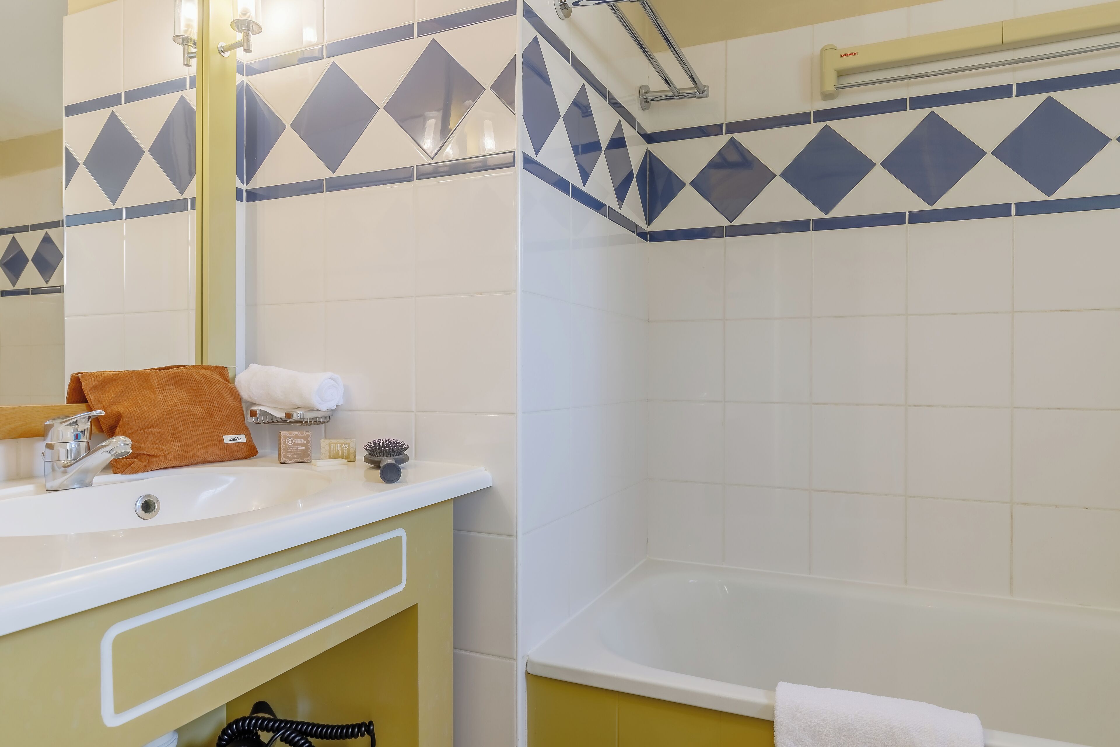 A bathroom with a white sink, mirror, and bathtub. There are towels and toiletries on the sink counter.