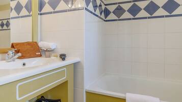 A bathroom with a white sink, mirror, and bathtub. There are towels and toiletries on the sink counter.