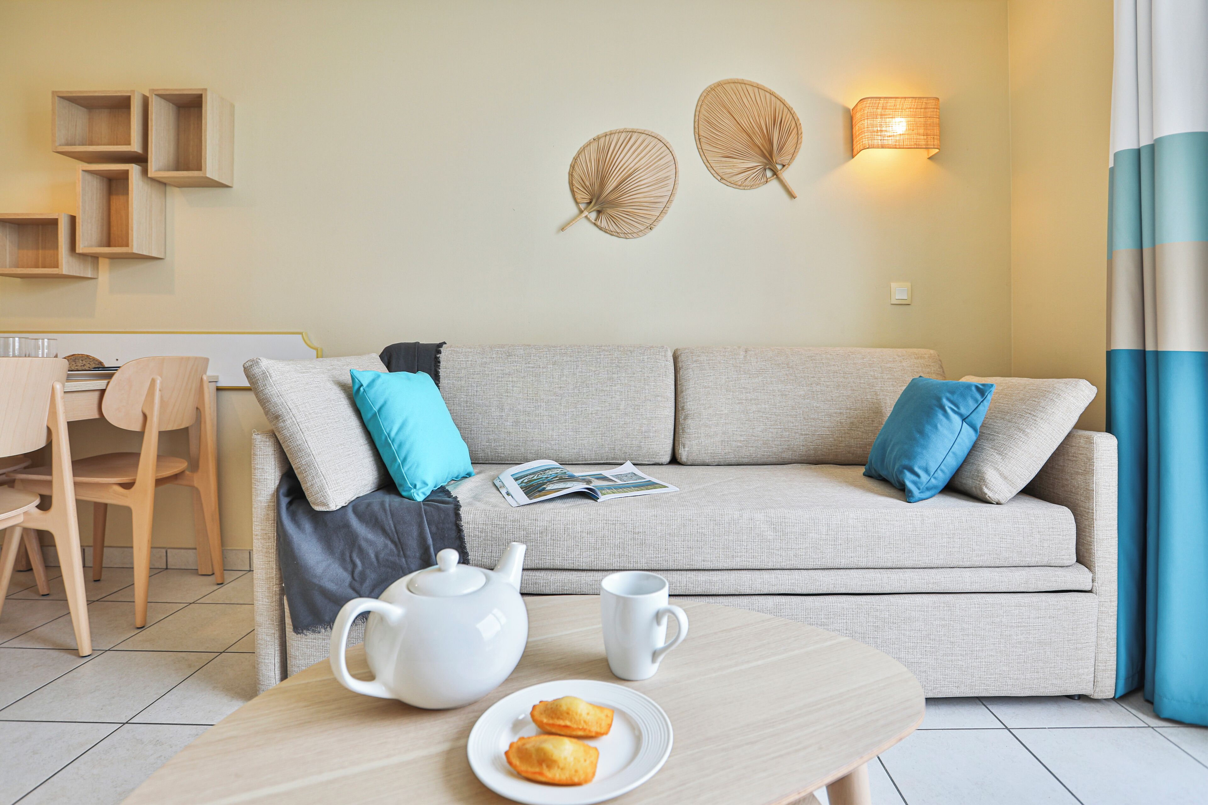 Ein modernes Wohnzimmer mit einer Couch, einem Tisch mit Teekanne und Gebäck, einem Sessel und Wanddekorationen.