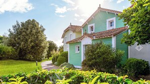 A two-story house with a green exterior and a tiled roof, surrounded by lush greenery and a clear sky. - Résidence Pierre & Vacances Le Domaine de Bourgenay (Talmont-Saint-Hilaire)