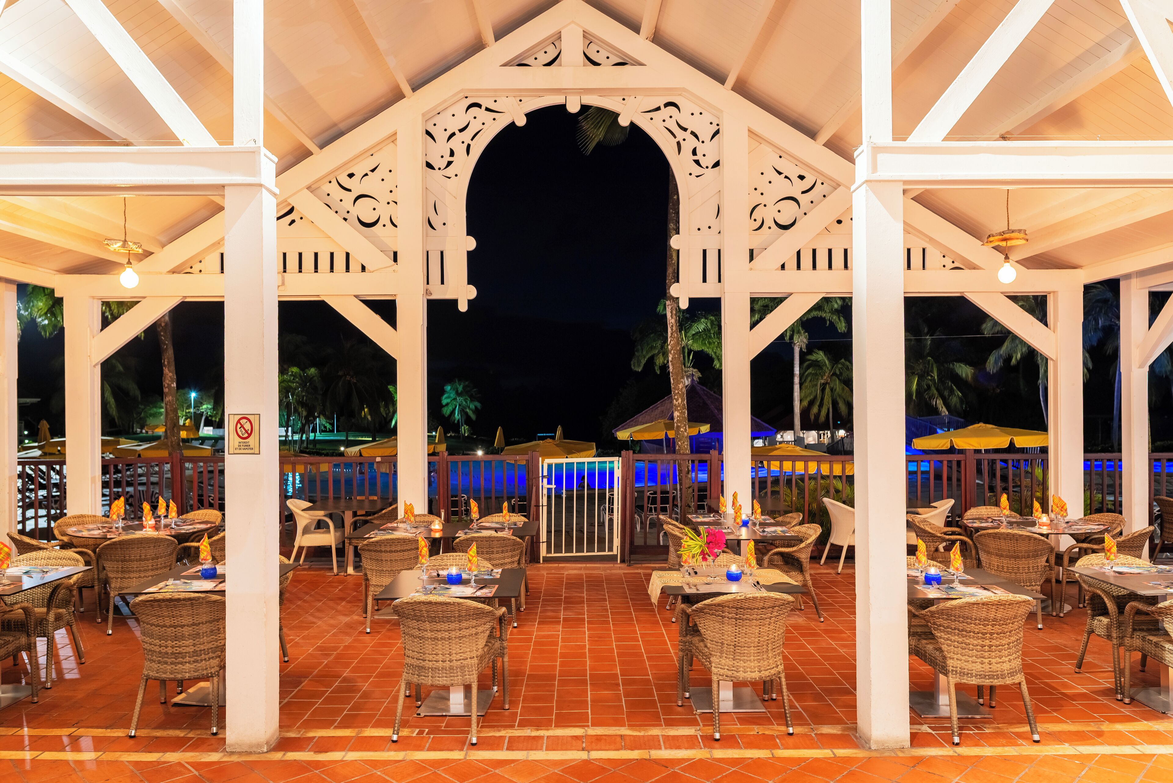 An outdoor restaurant with wicker furniture, a covered patio, and a view of the night sky.
