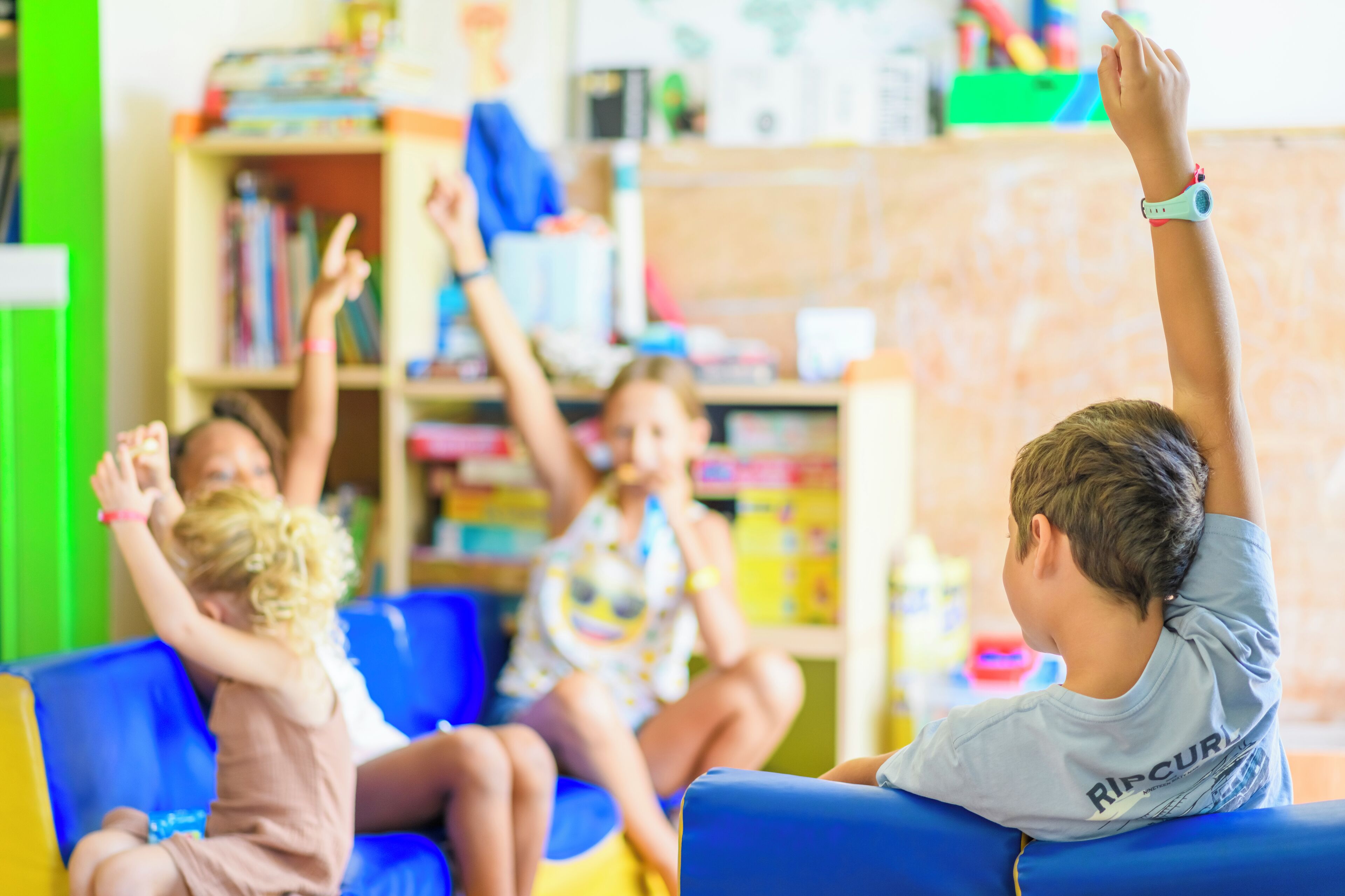 A child in a classroom with a blue chair, a bookshelf, and educational materials in the background.