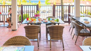An outdoor dining area with wicker chairs and tables, overlooking a beach with palm trees and a clear sky. - Village St Luce Pierre & Vacances (Sainte-Luce)