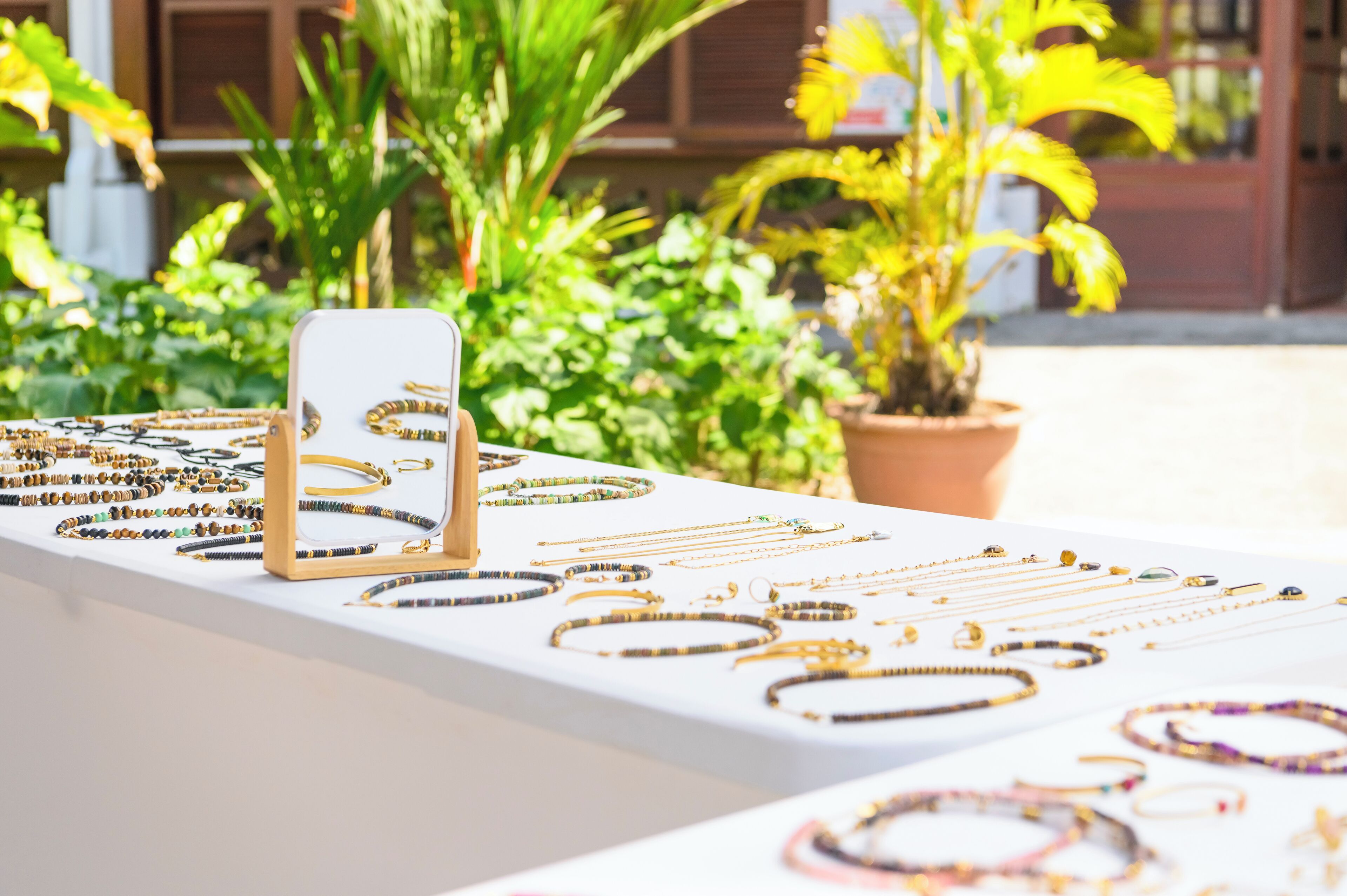 Una exhibición de joyería con varios collares y pulseras sobre una mesa blanca, rodeada de plantas verdes.