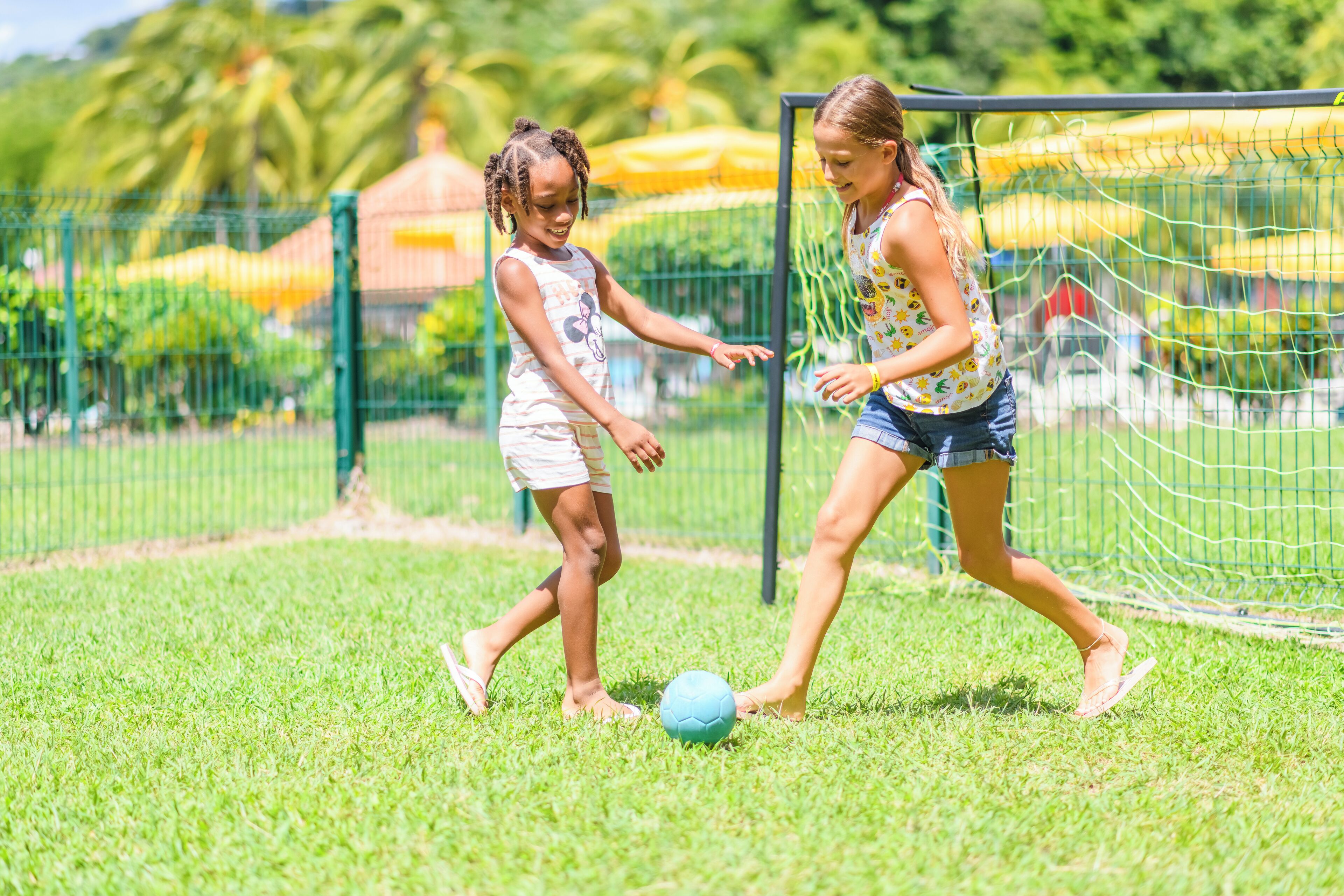 Two children playing soccer on a grassy field with a goalpost in the background.