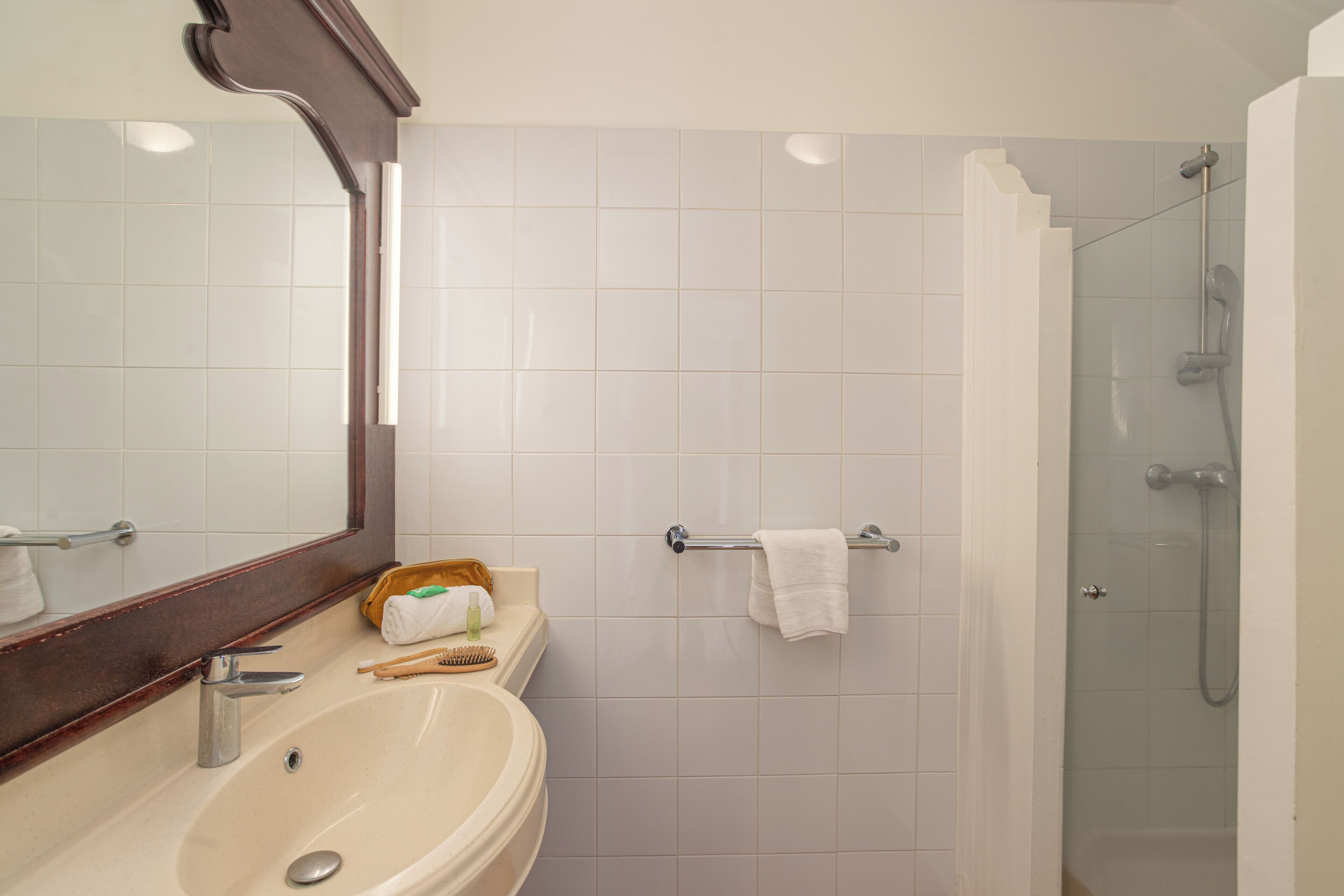A bathroom with a sink, mirror, towel rack, and shower.