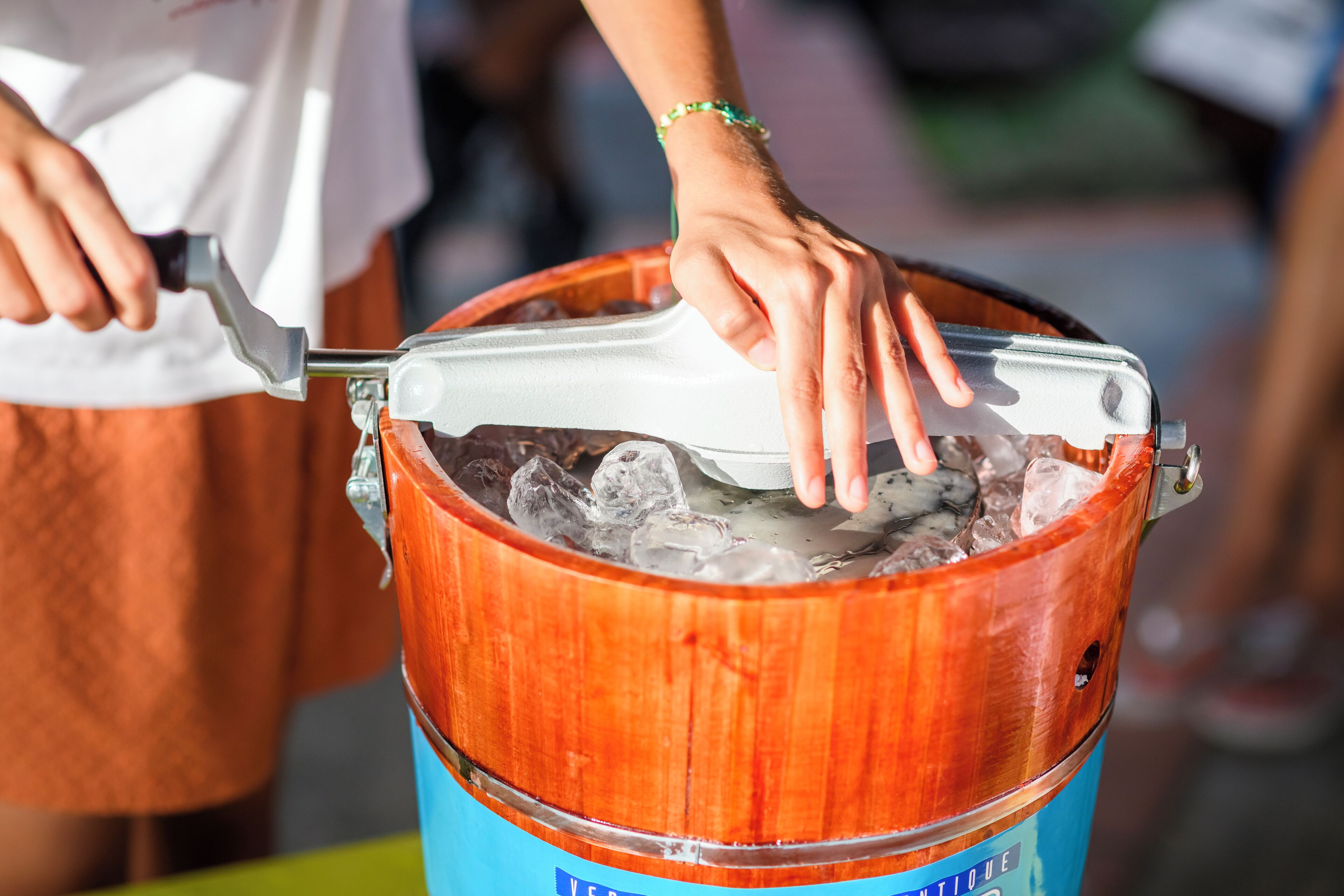 A wooden bucket with a metal scoop, containing ice and a beverage.