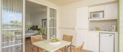 A compact kitchen with a microwave and dishwasher, a dining area with wicker chairs, and a sliding glass door leading to a balcony.