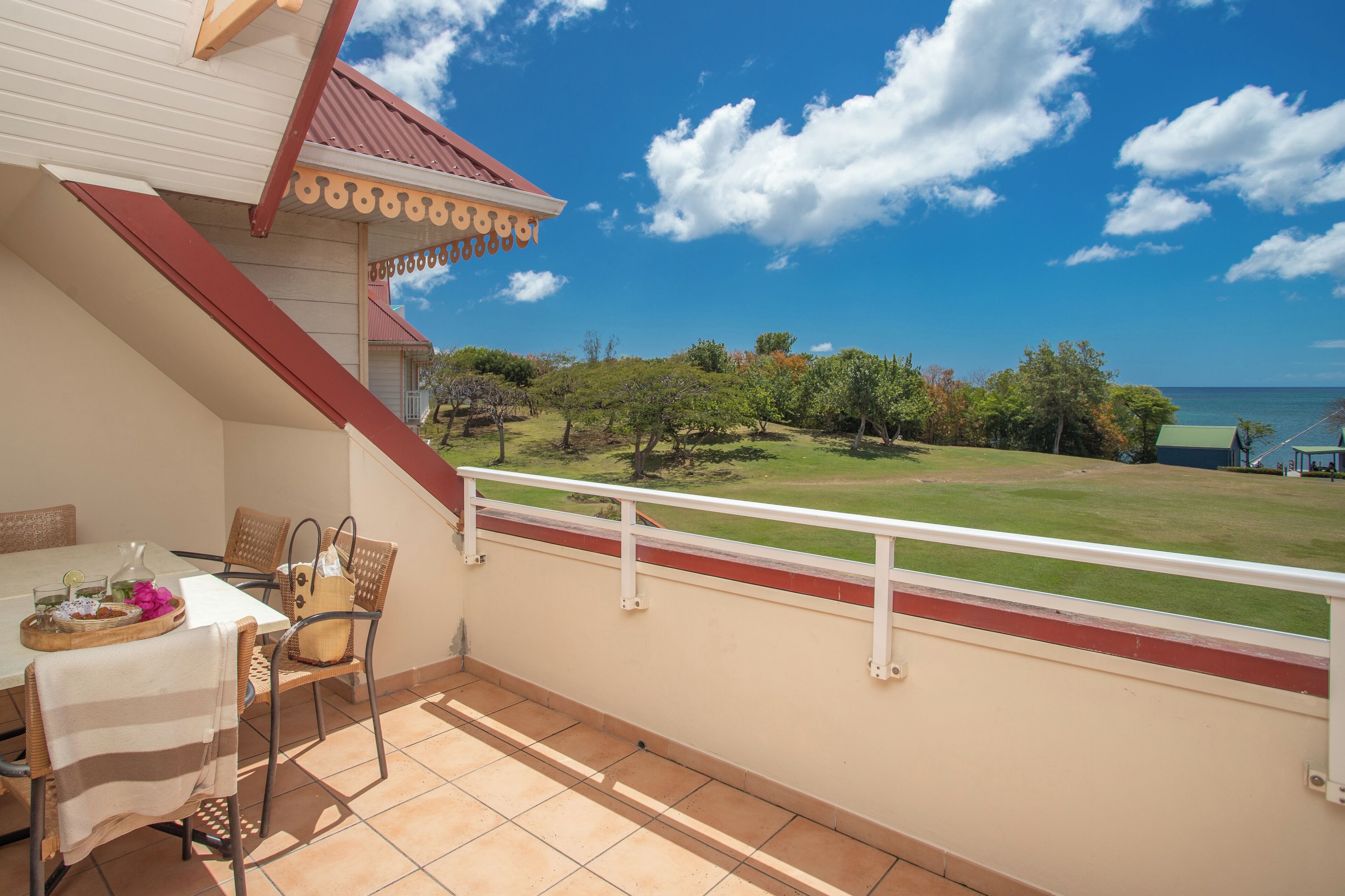 A balcony with a table and chairs, overlooking a grassy area and the sea.