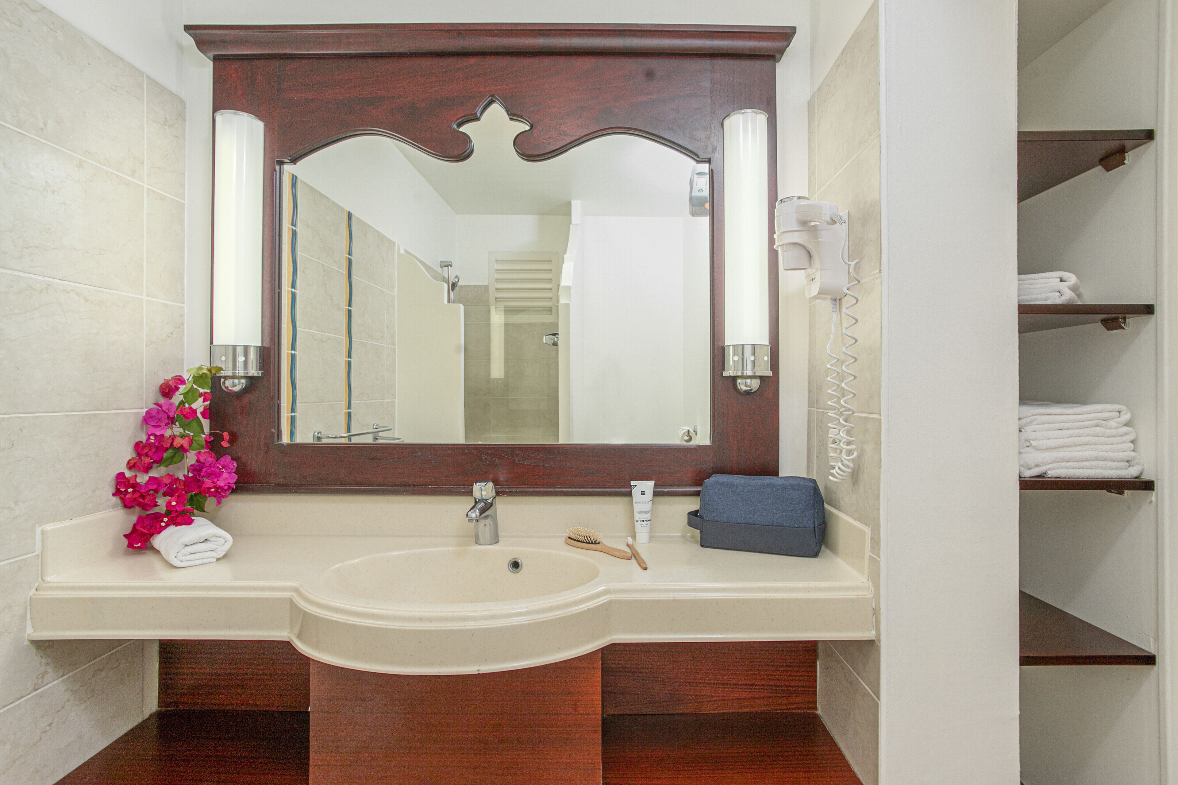 Une salle de bain avec un grand miroir, un lavabo, un porte-serviettes et une étagère où sont pliés les serviettes.