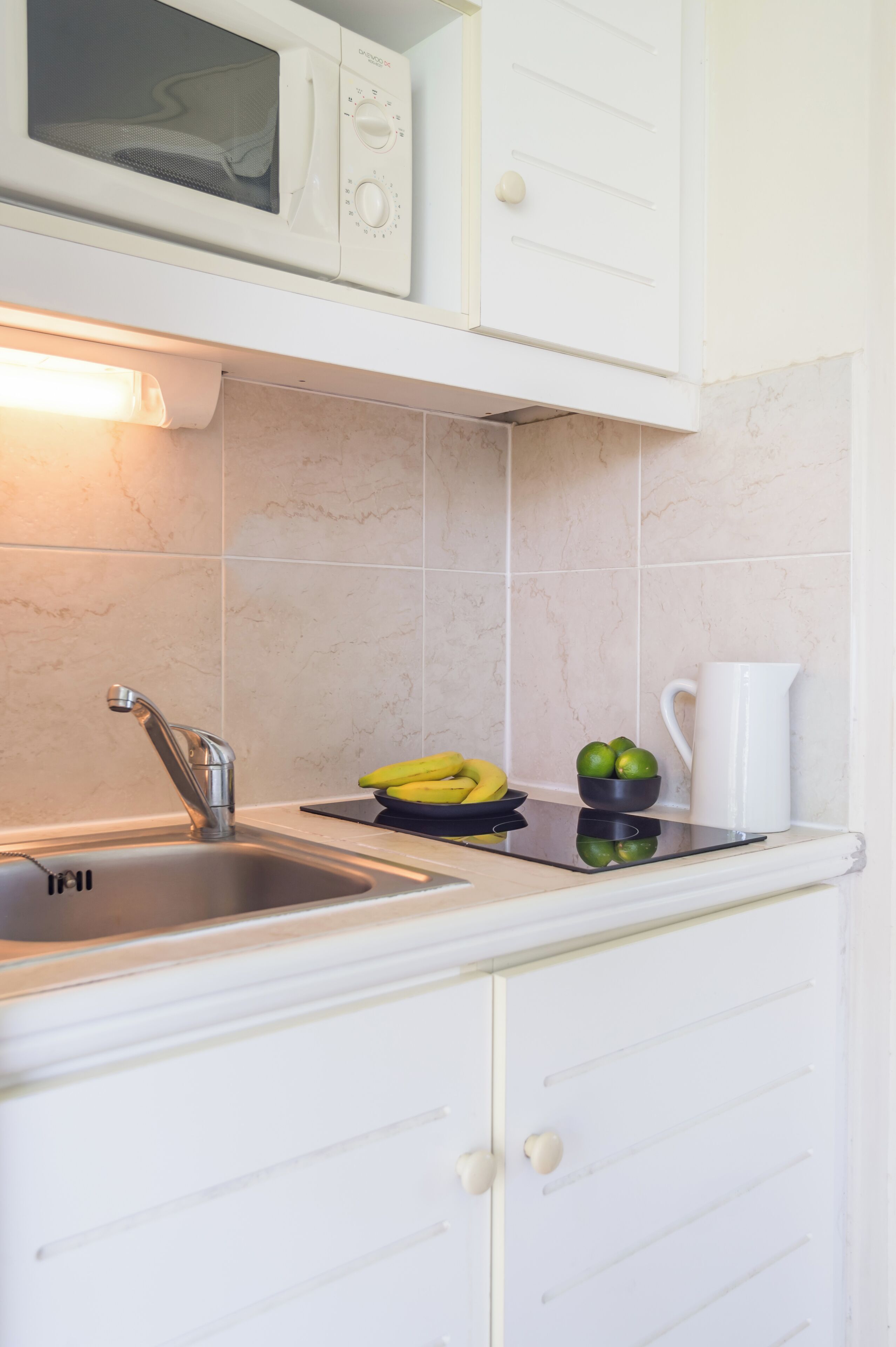 A kitchen with a microwave, sink, and a bowl of bananas and limes on the counter.