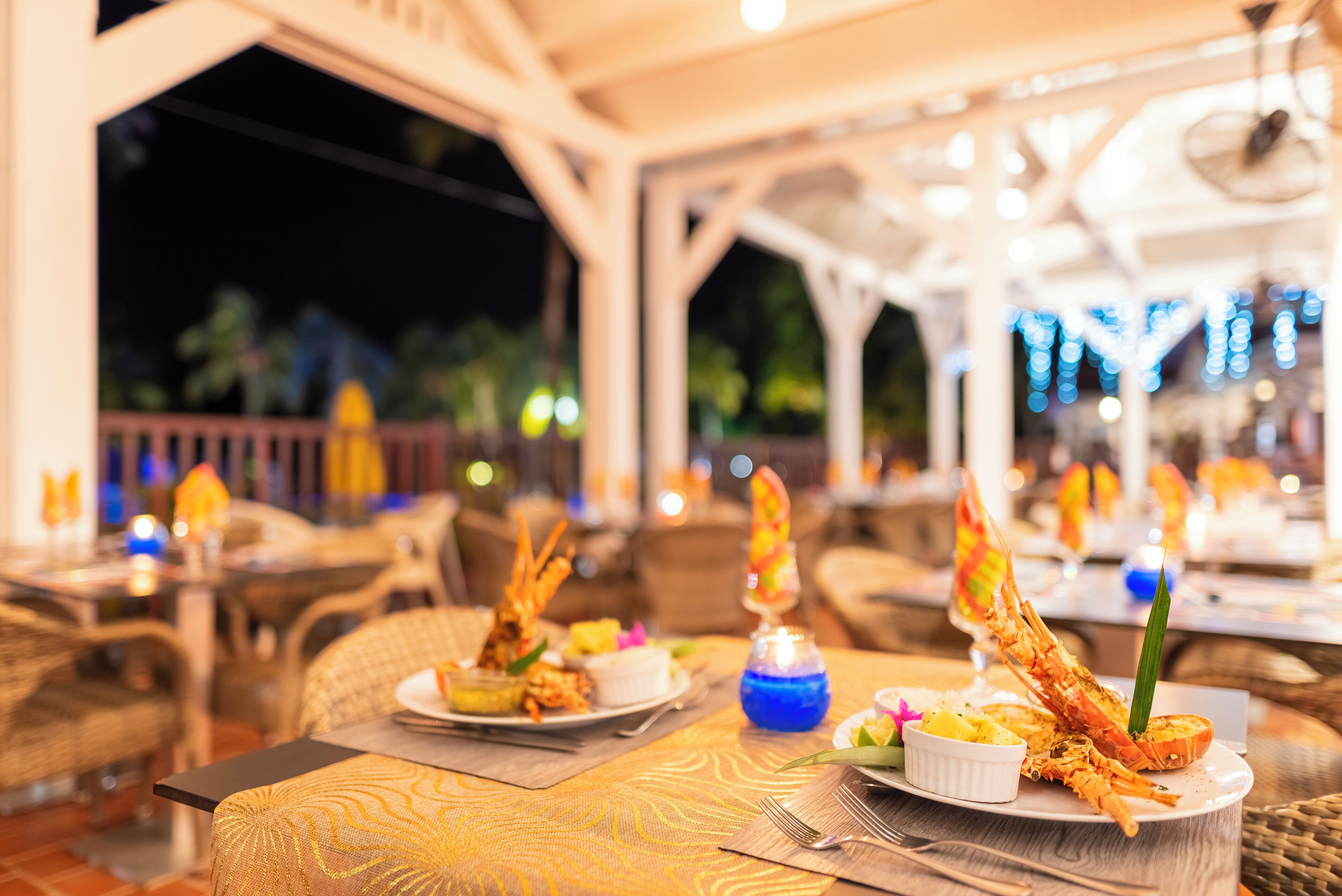 Un restaurant où les tables sont dressées pour le service, proposant des plats de fruits de mer et offrant une ambiance tropicale.