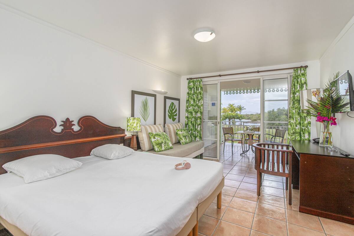A bedroom with a bed, a desk, and a balcony with a view.