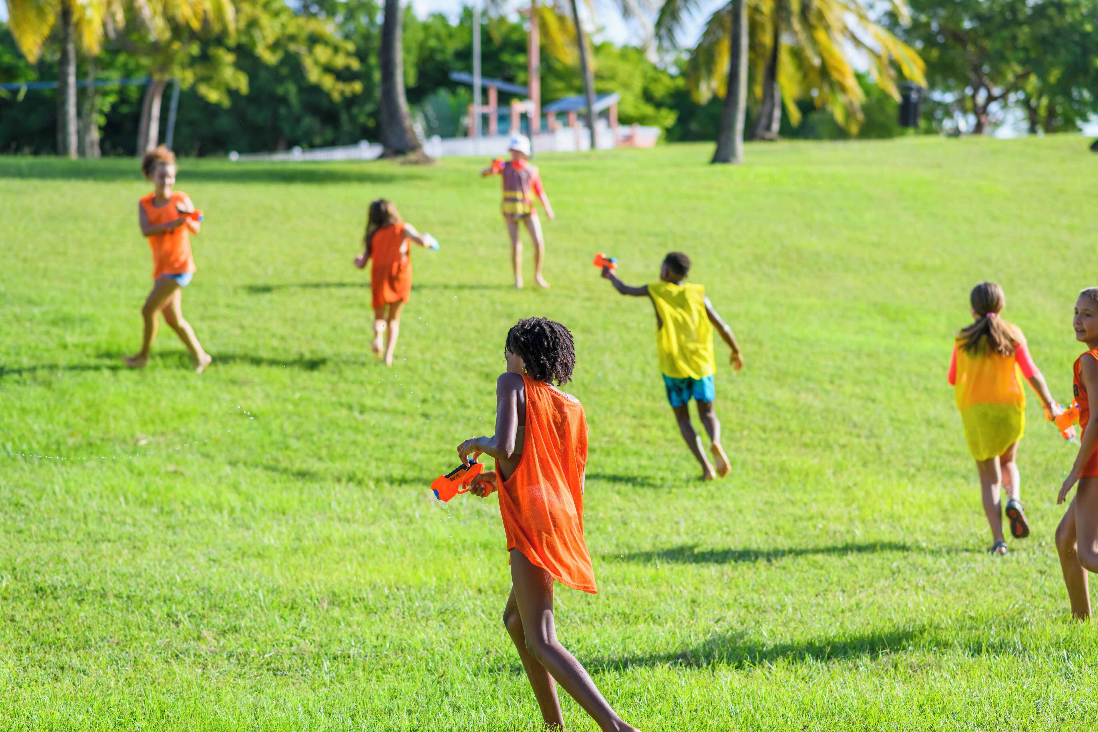 A group of people in a grassy field, some holding water guns.