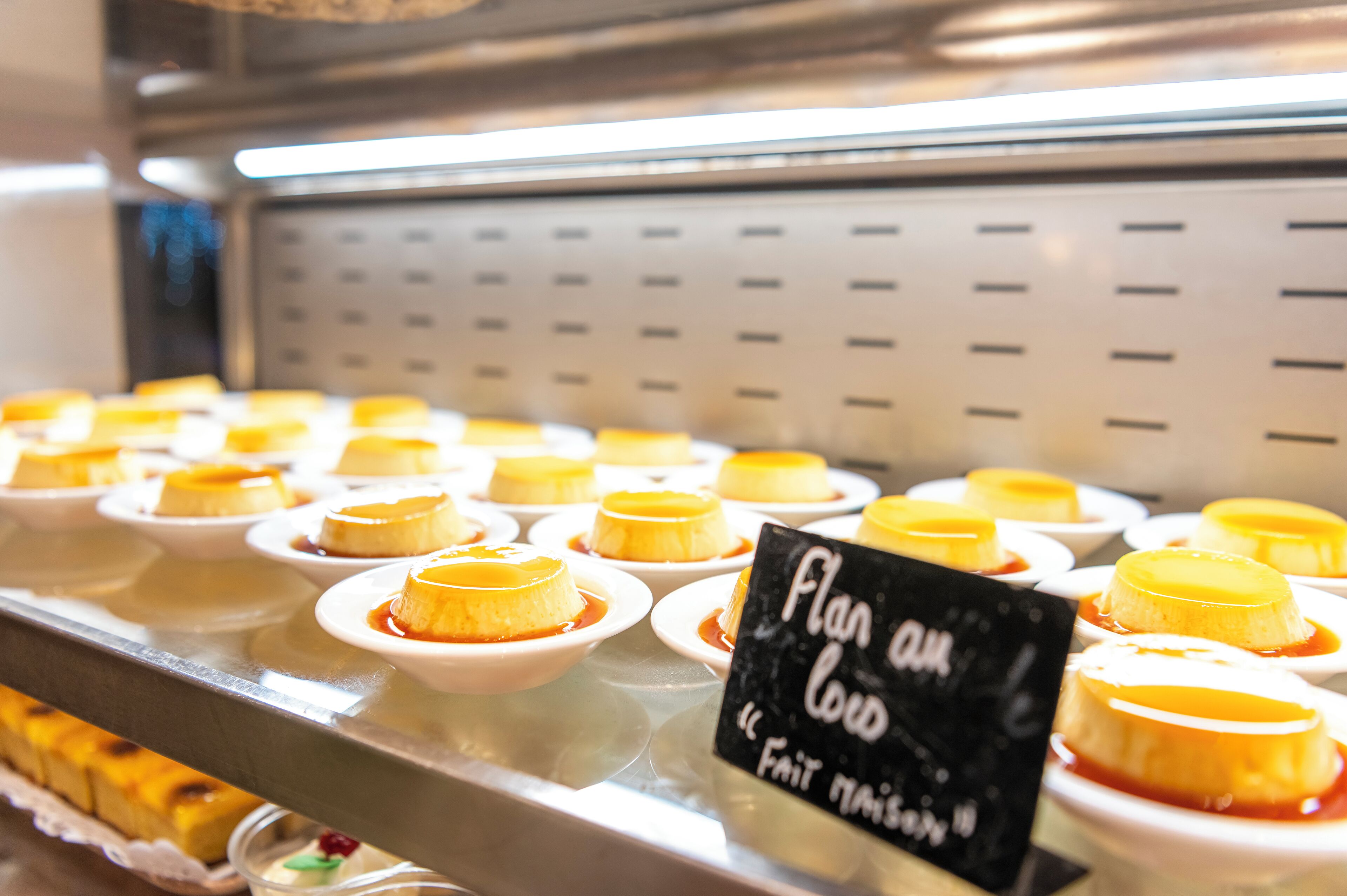 A display of flan desserts in small white bowls, arranged on a metal counter with a sign that reads "Flan au Lard."