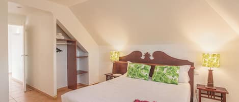 A bedroom with a bed, two bedside lamps, a nightstand, a closet, and a door leading to another room.