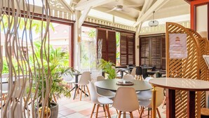A restaurant with round tables and chairs, potted plants, and wooden lattice screens. - Village St Luce Pierre & Vacances (Sainte-Luce)
