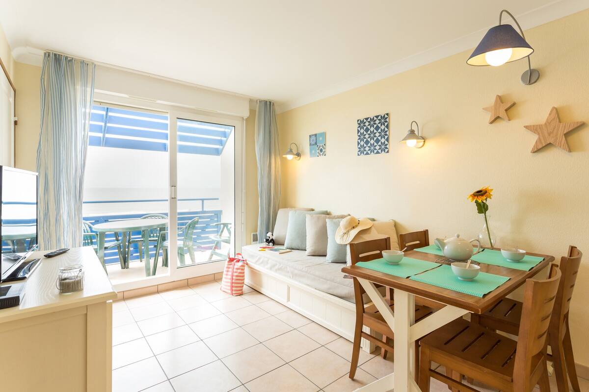 Une pièce lumineuse avec un balcon, une table à manger avec des chaises, un canapé et un bureau avec un ordinateur.