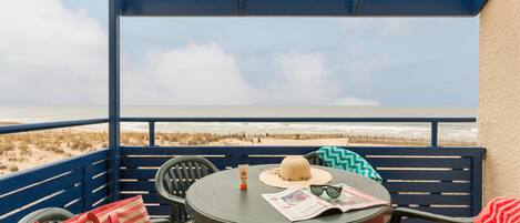 A balcony with a view of the beach, featuring a table with a hat, sunglasses, and a striped bag.