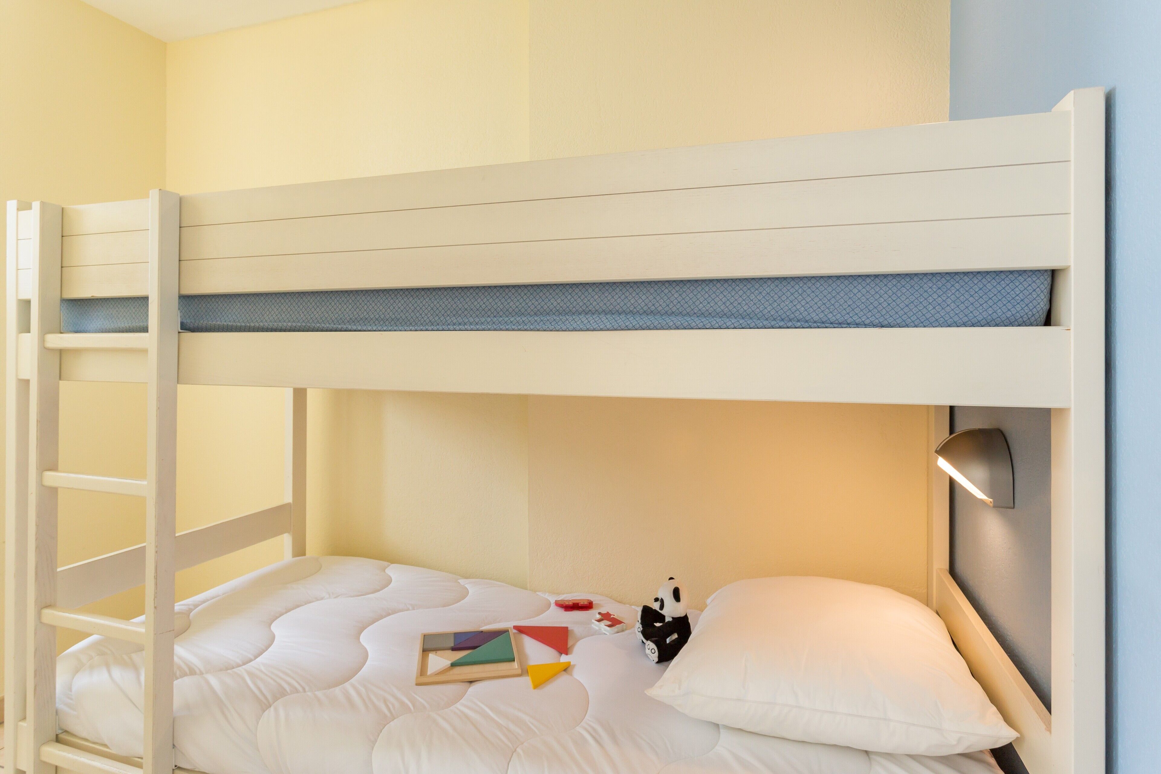 Una cama litera con escalera, una mesita de noche con lámpara y un almohadón.