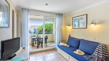 A living room with a TV, a sofa, a table, and a balcony with a view.